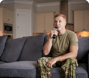 man in camo outfit on gray couch using dish voice remote